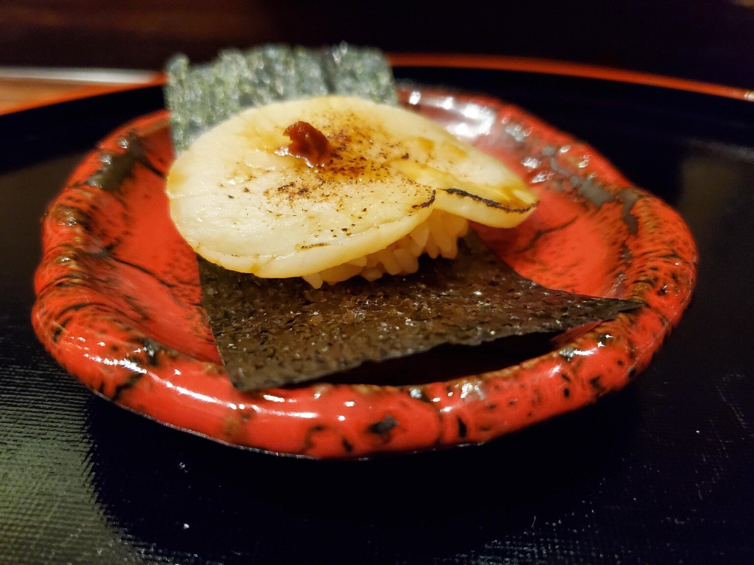 Seared nigiri presented on a red lacquer plate